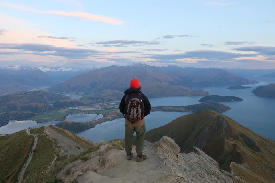Standing on a mountain summit at dusk, overlooking a lake and mountain range